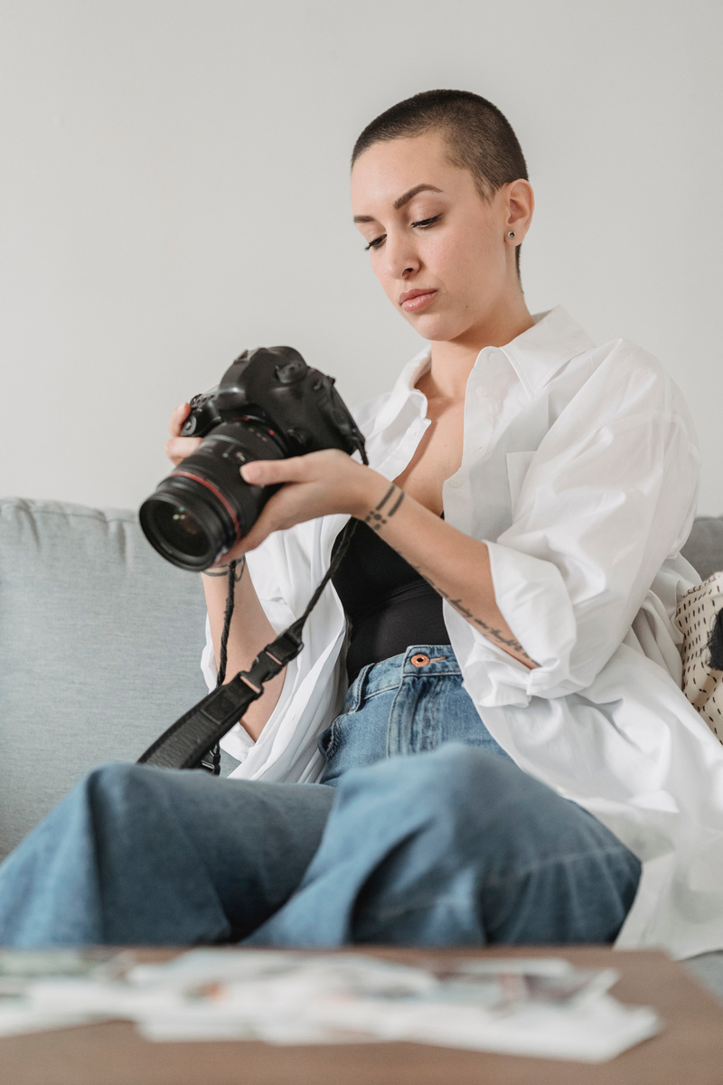 Photographer with digital photo camera on sofa in room